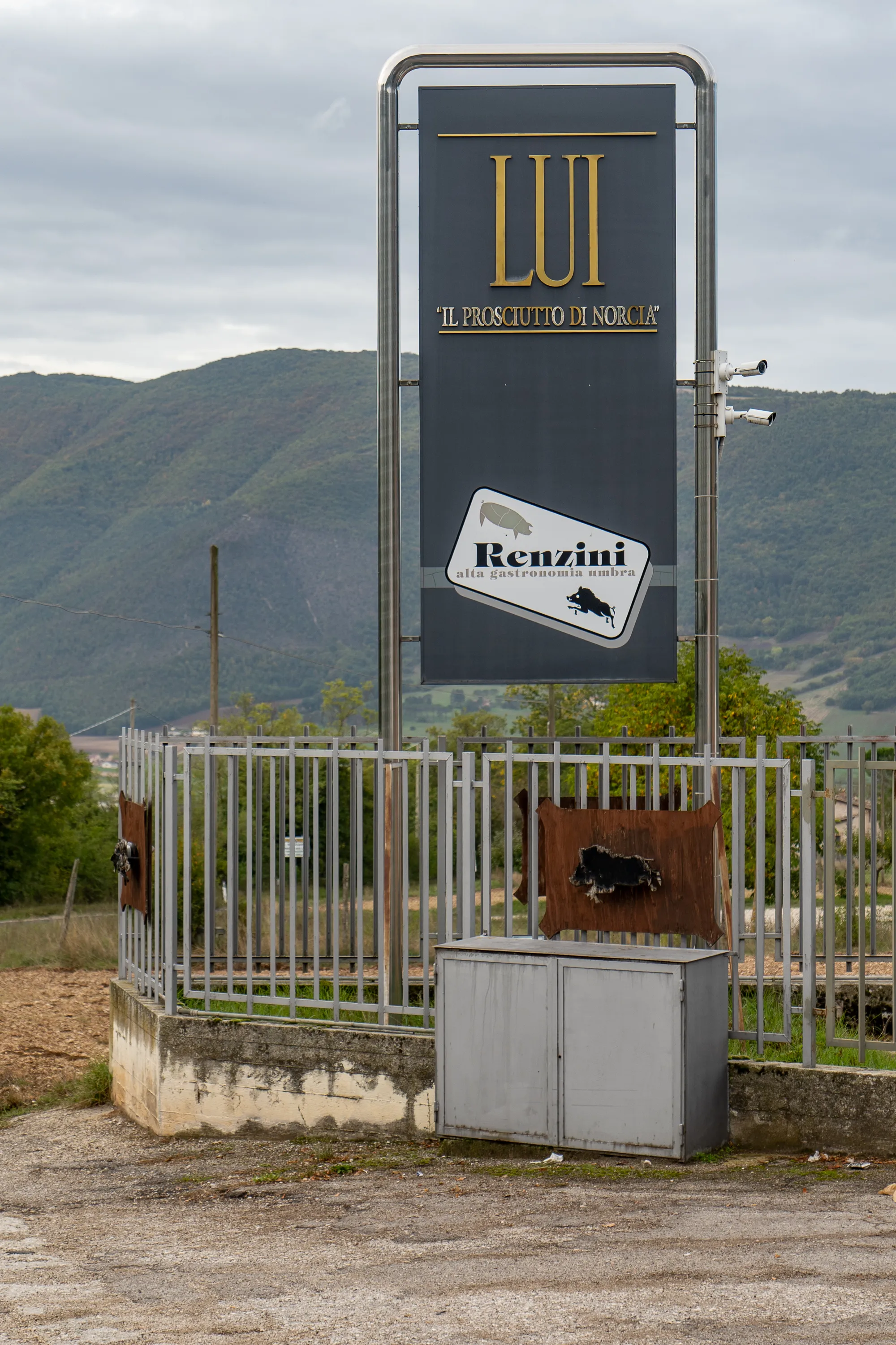 Schild für Prosciutto di Norcia in hügeliger Landschaft