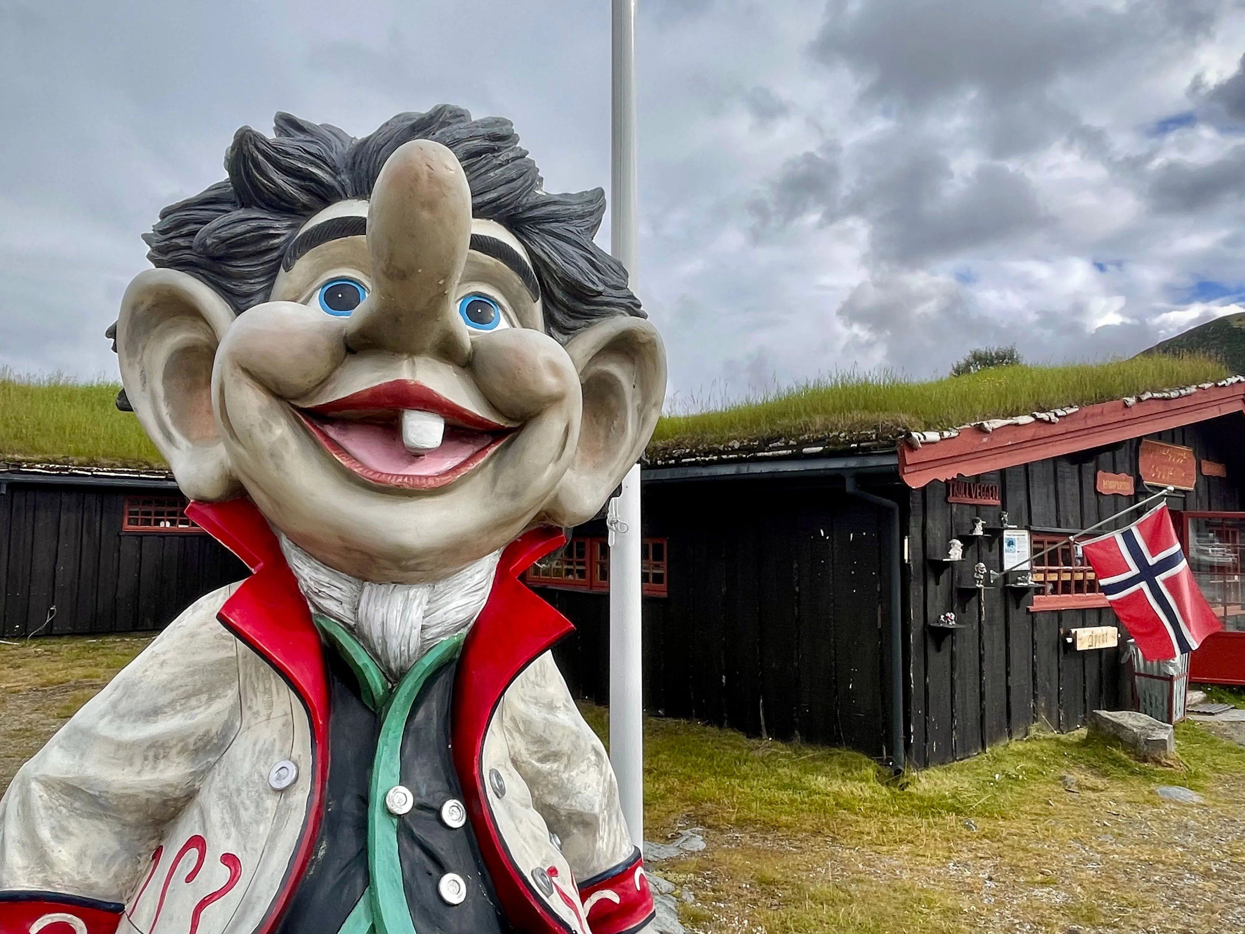 große skulptur eines lächelnden menschen mit roter flagge und grasdachhaus im hintergrund