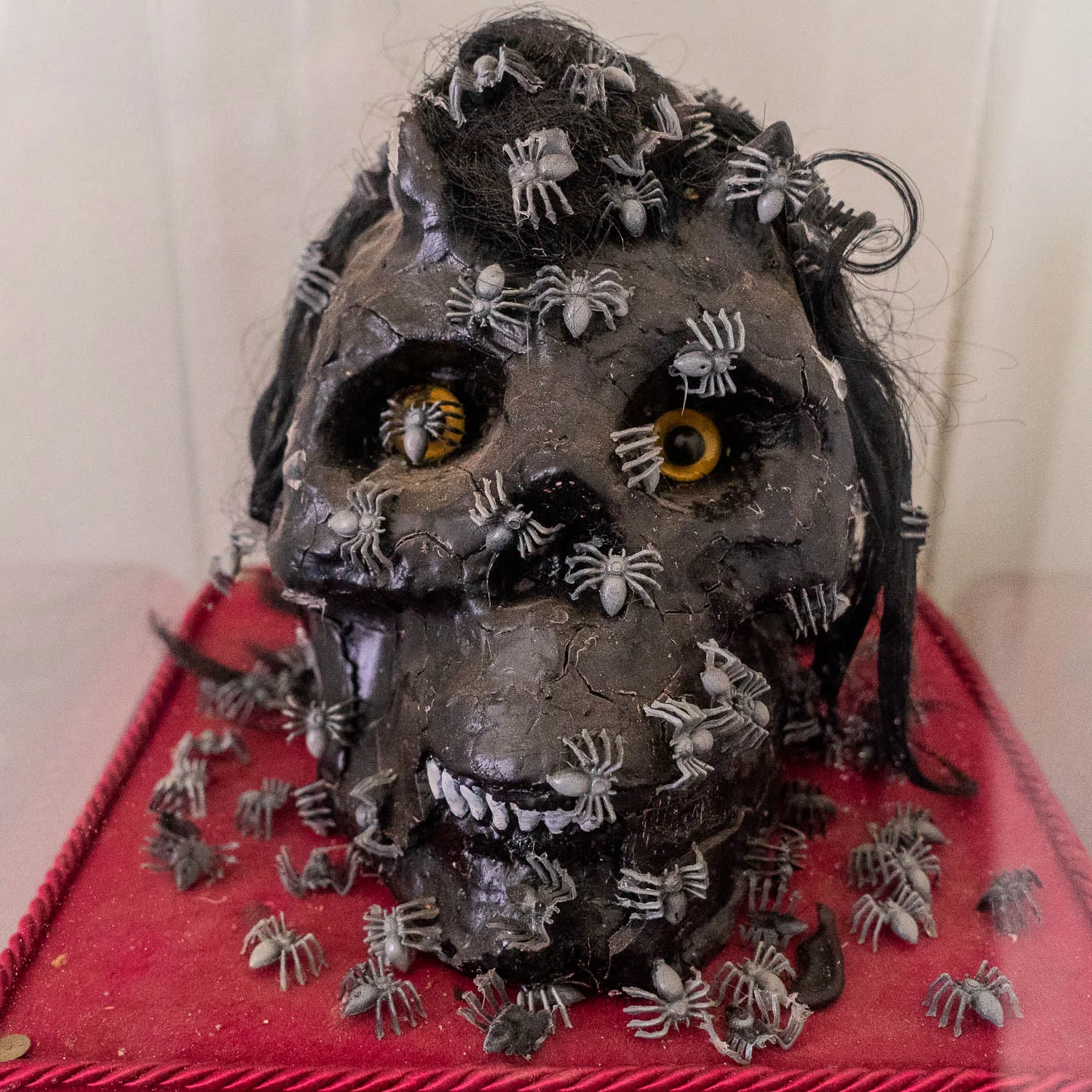 Skulptur eines schädelartigen Kopfes mit vielen Spinnen und gelben Augen