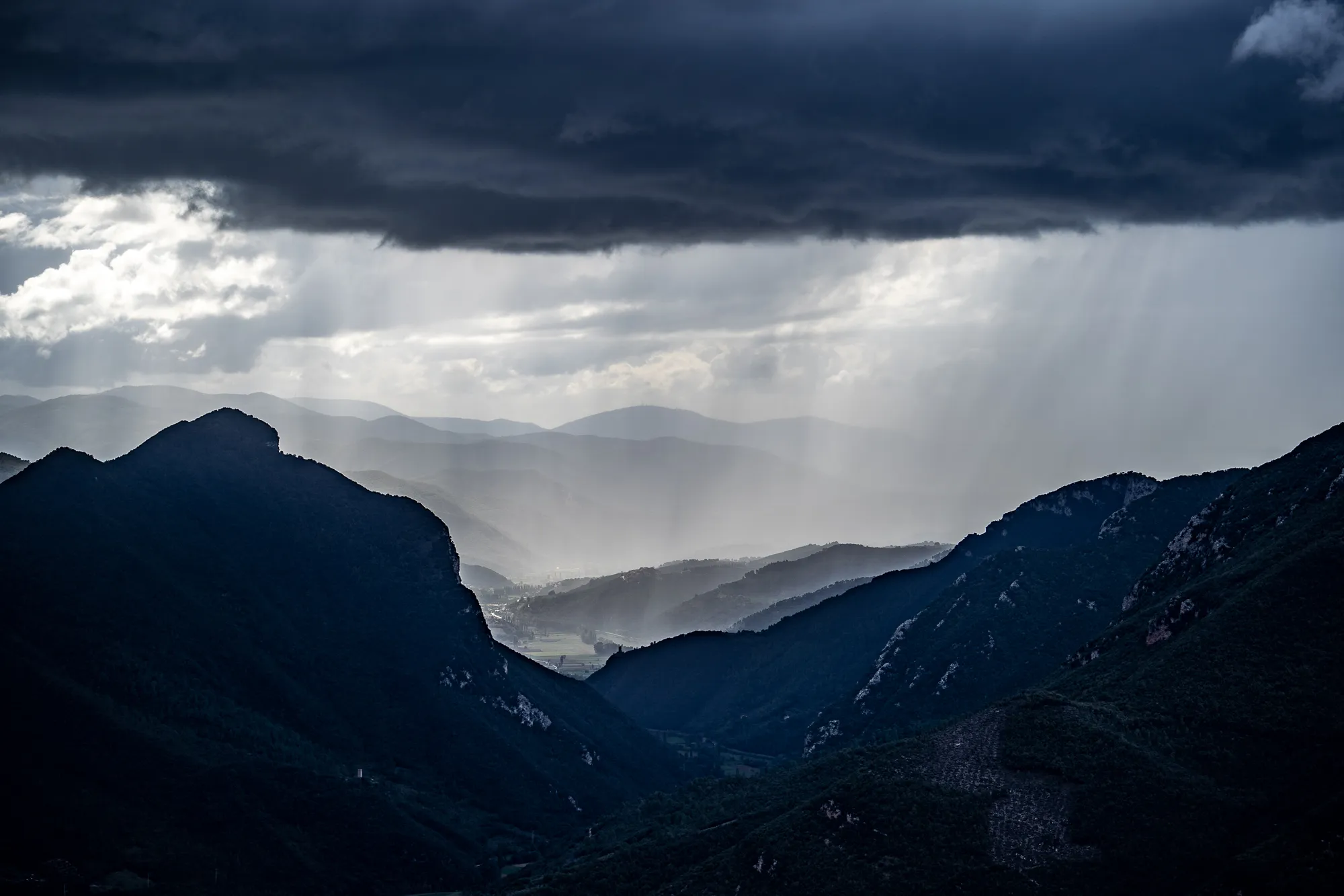 Regenstrahlen durch Wolken über bewaldeten Bergen in Umbrien