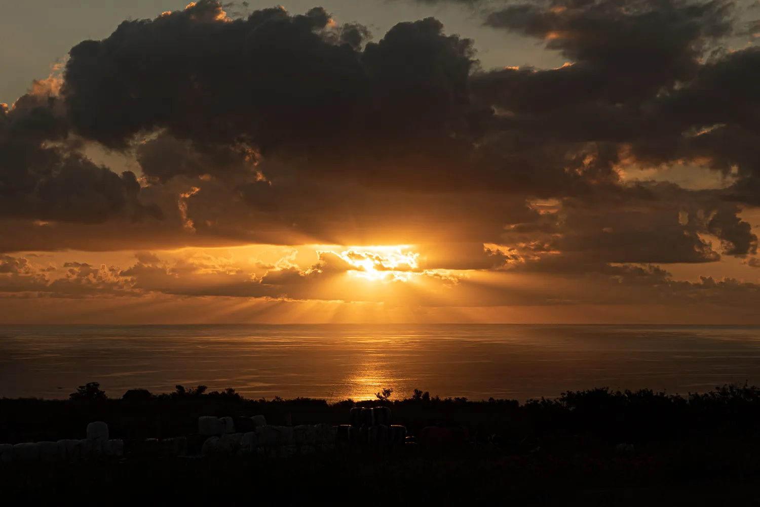 Sonnenuntergang mit Strahlen über Meer und dunklen Wolken