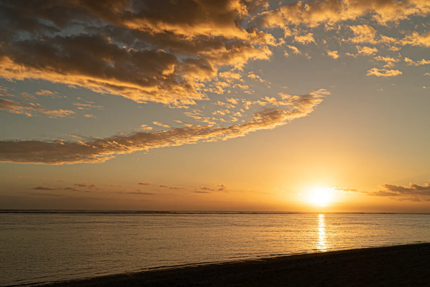 Sonnenuntergang über ruhigem Wasser mit goldenen Wolken am Horizont