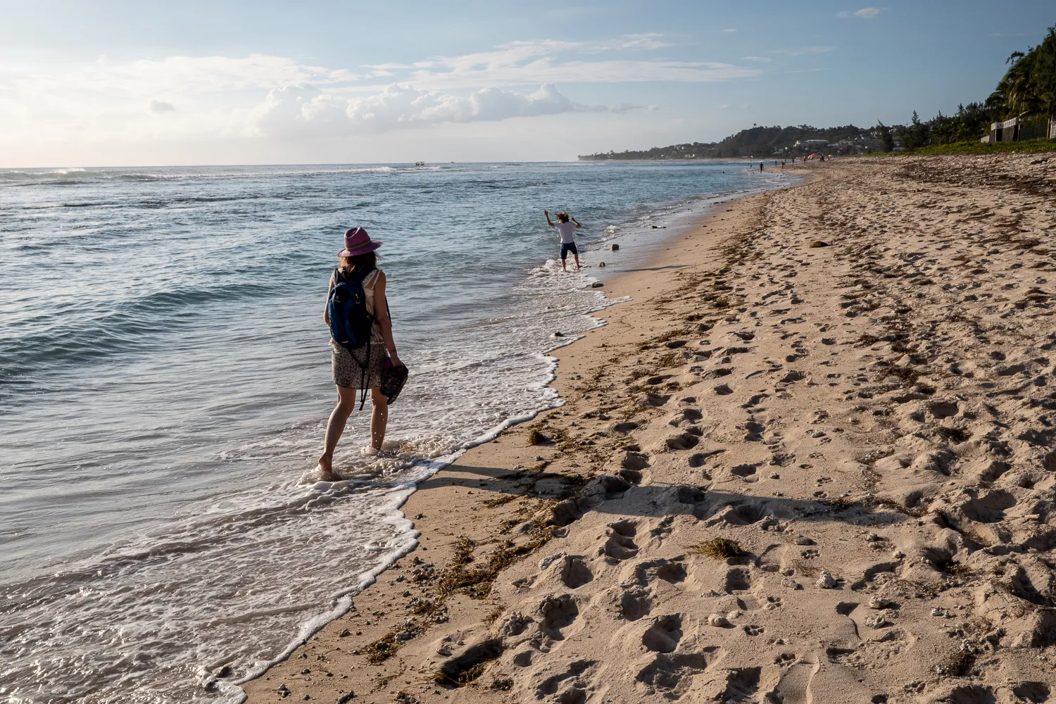 Zwei Personen spazieren am Strand entlang, wobei eine im Wasser steht und die andere auf dem Sand.
