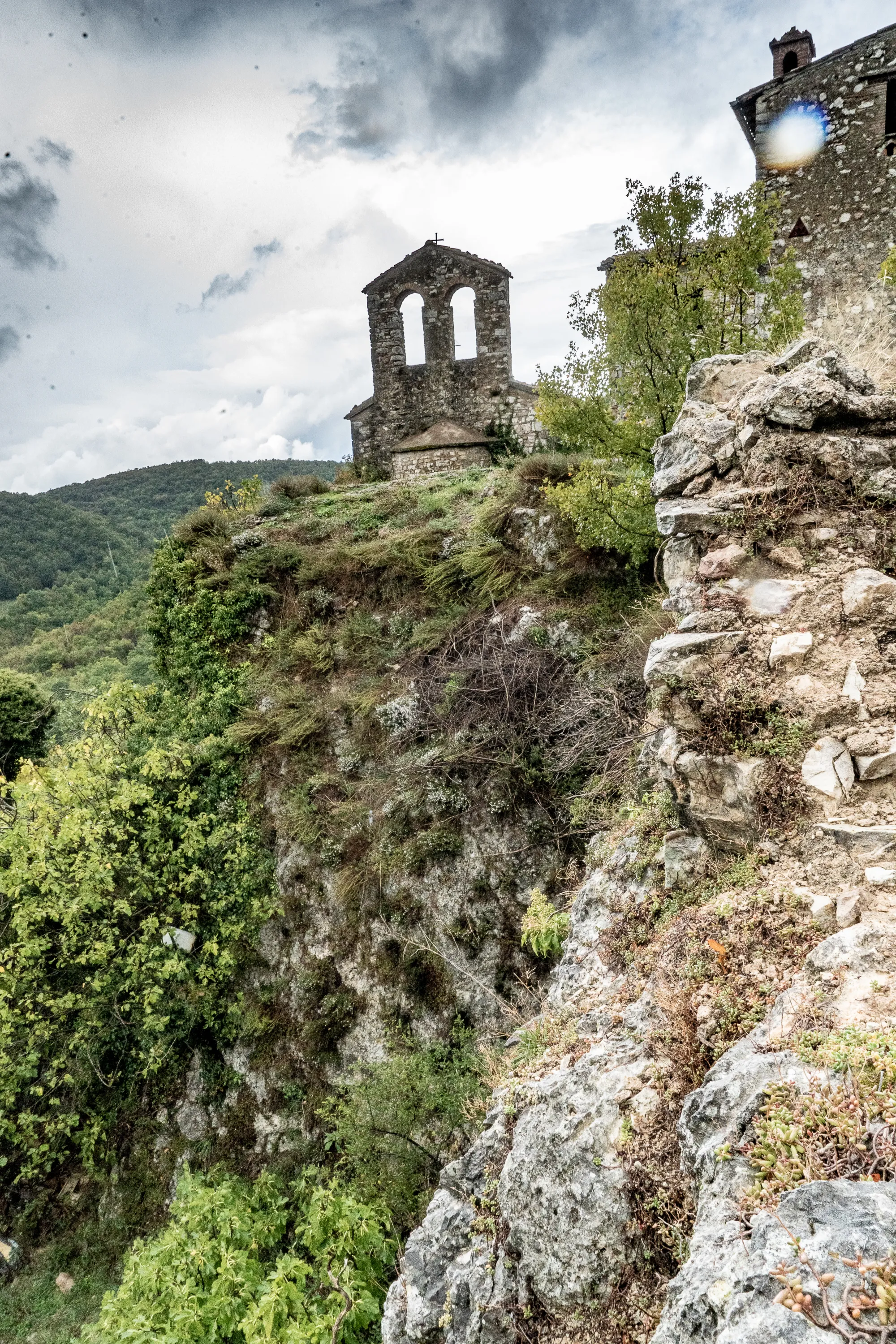 Alter Steinbau auf felsigem Berg mit üppiger Vegetation und bewölktem Himmel