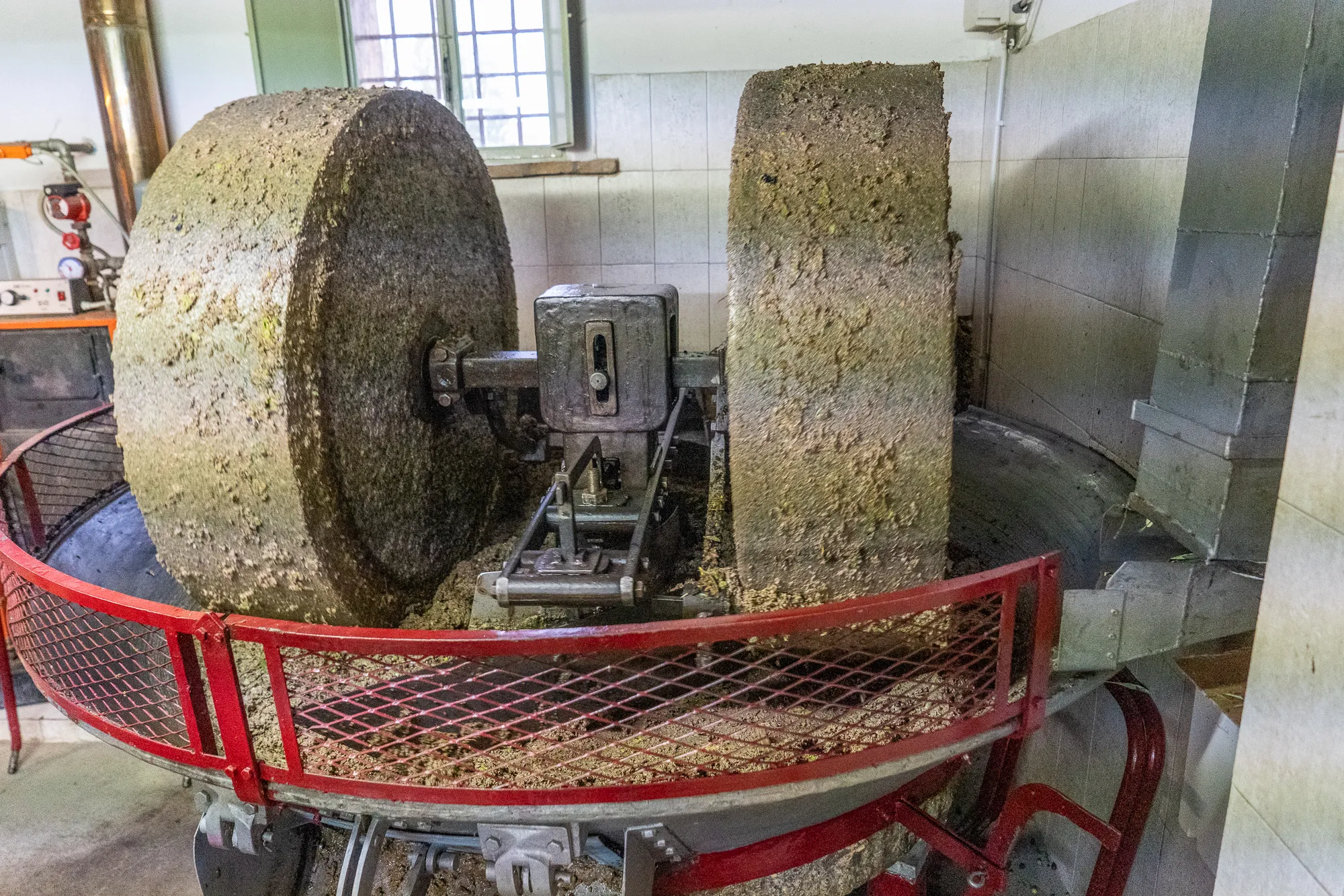 Zwei große Steinmühlenrädchen in einer Werkstatt mit rotem Metallgeländer.