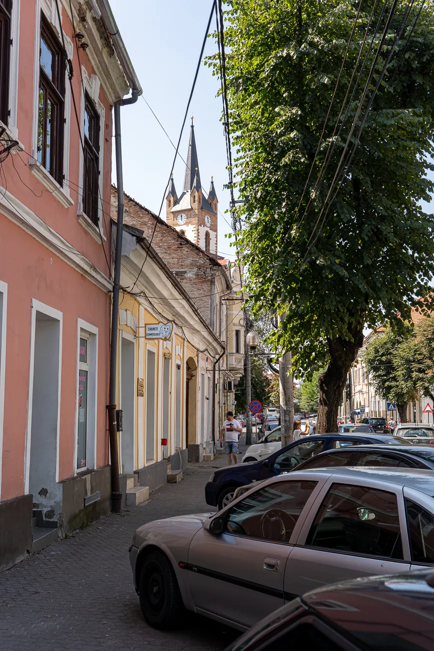 Straße mit geparkten Autos und Kirchturm im Hintergrund