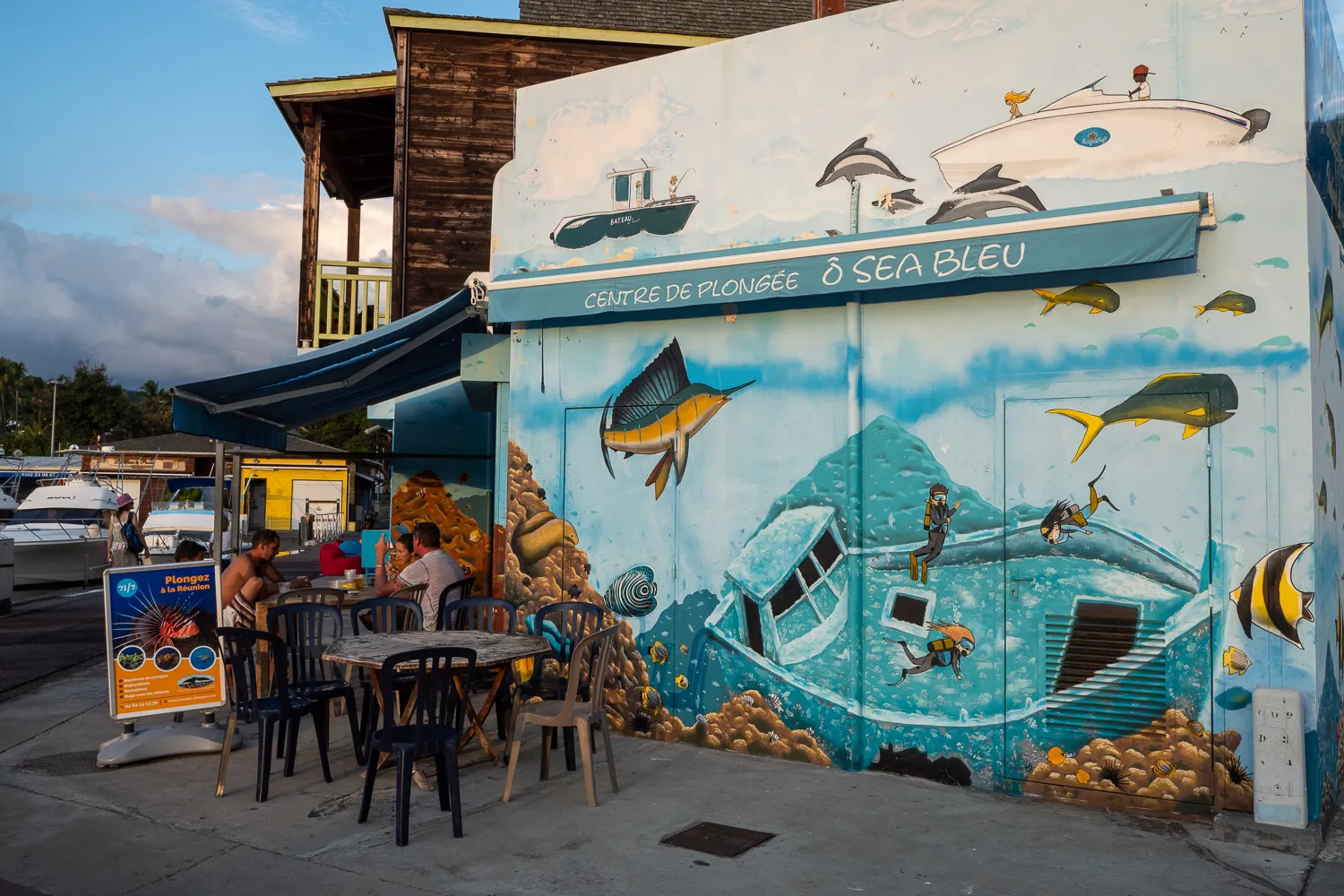 Mural an einer Wand mit Tauchcenter und Meerestieren, Menschen sitzen draußen.