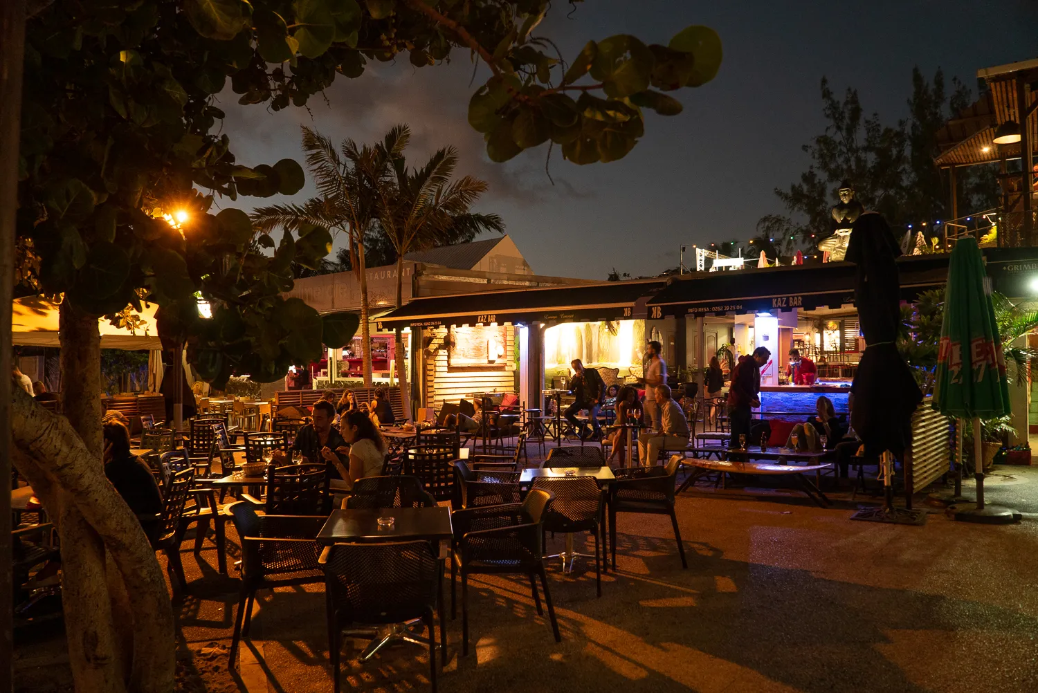 Nachtbeleuchtete Terrasse mit Tischen, Stühlen und Palmen im Freien