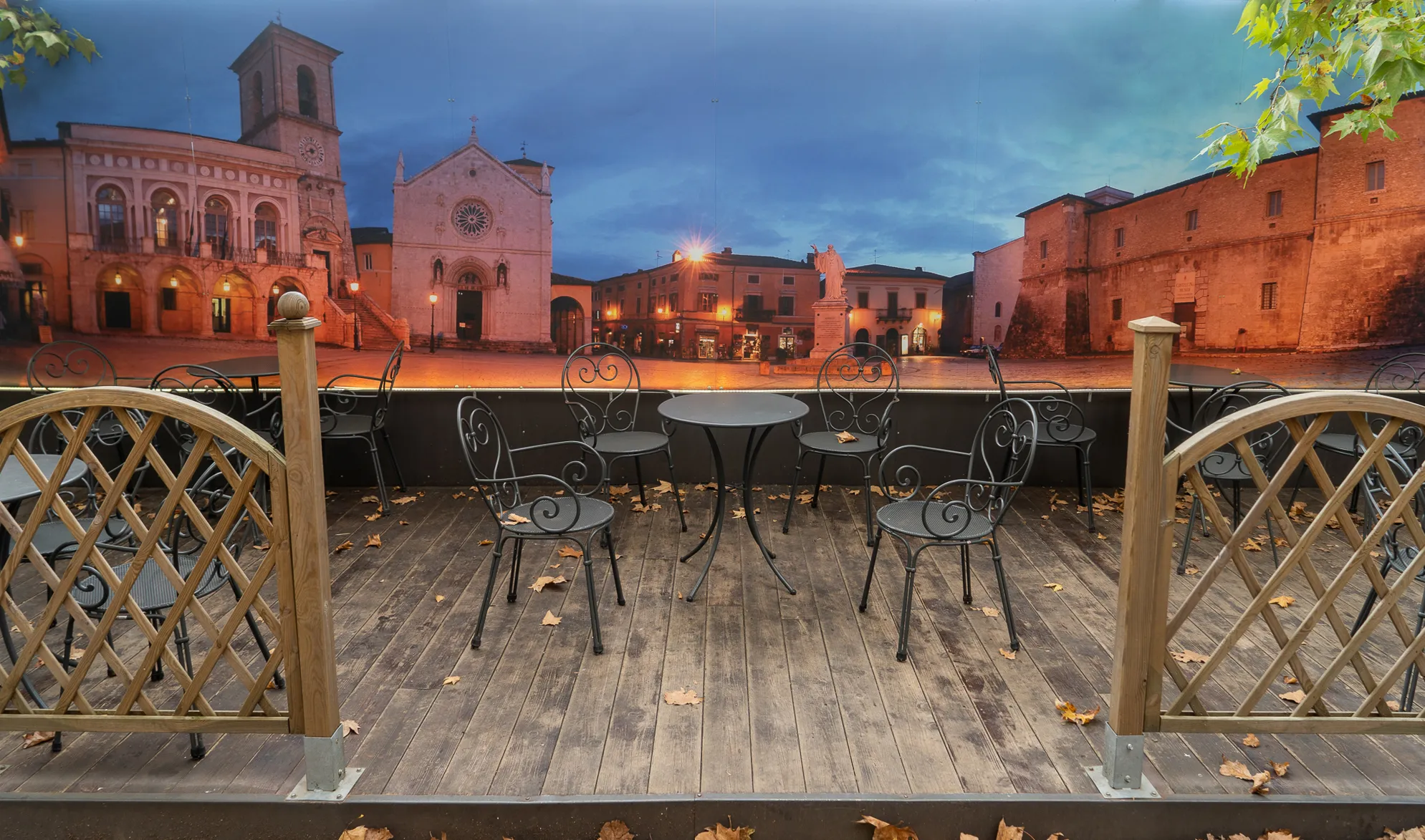 Terrasse mit Tischen und Stühlen, Blick auf beleuchtete historische Gebäude im Zentrum von Norcia.