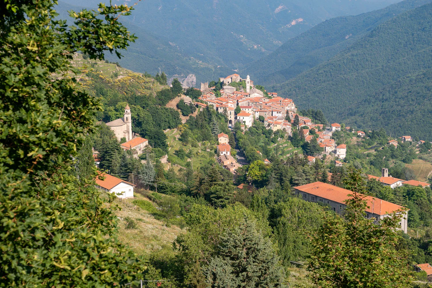 Dorf mit roten Dächern und Kirche auf grünen Hügeln