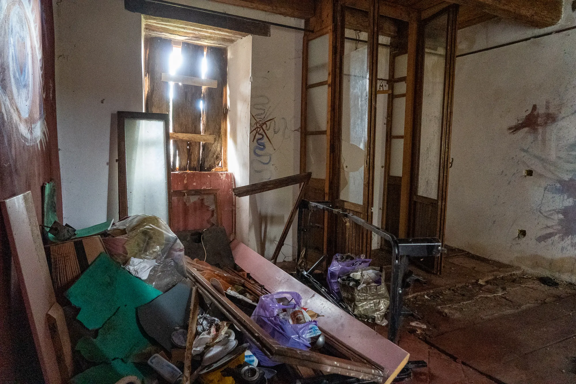 Verlassener Raum mit Müll und zerstörten Möbeln, Licht fällt durch Fenster.