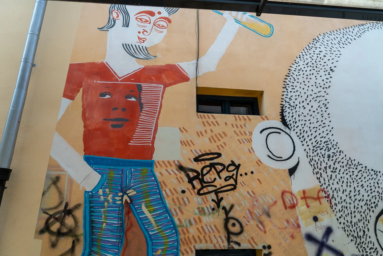 Farbiger Wandgemälde mit stilisierten Figuren und Graffiti auf gelber Fassade