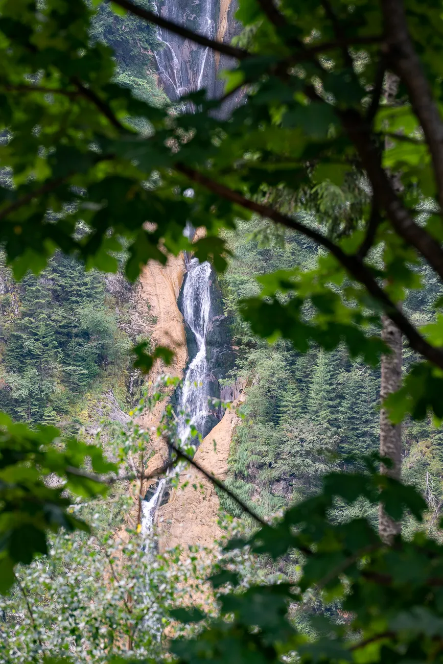 Wasserfall fällt durch grünen Wald, teilweise von Blättern verdeckt