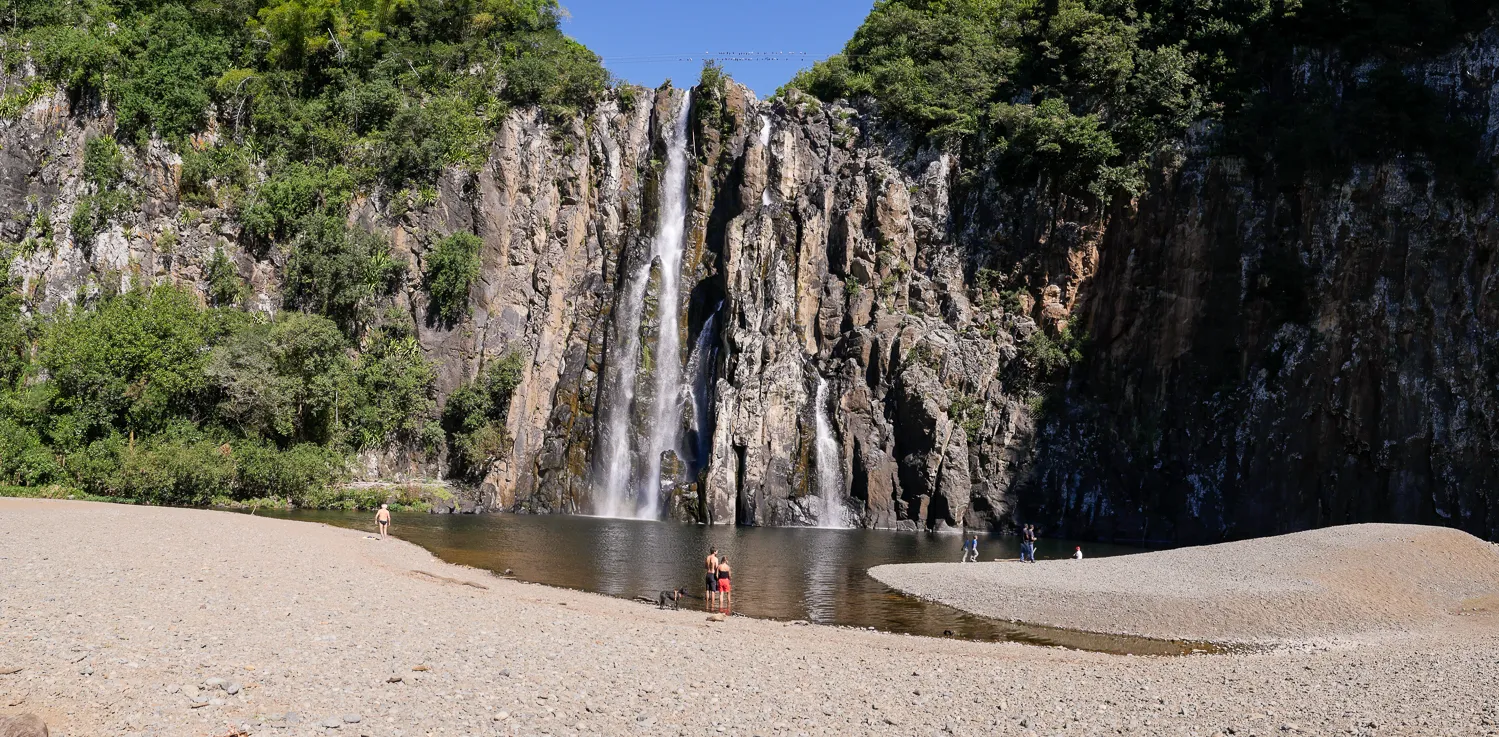 Wasserfall fällt in einen See, umgeben von Felsen und Bäumen.