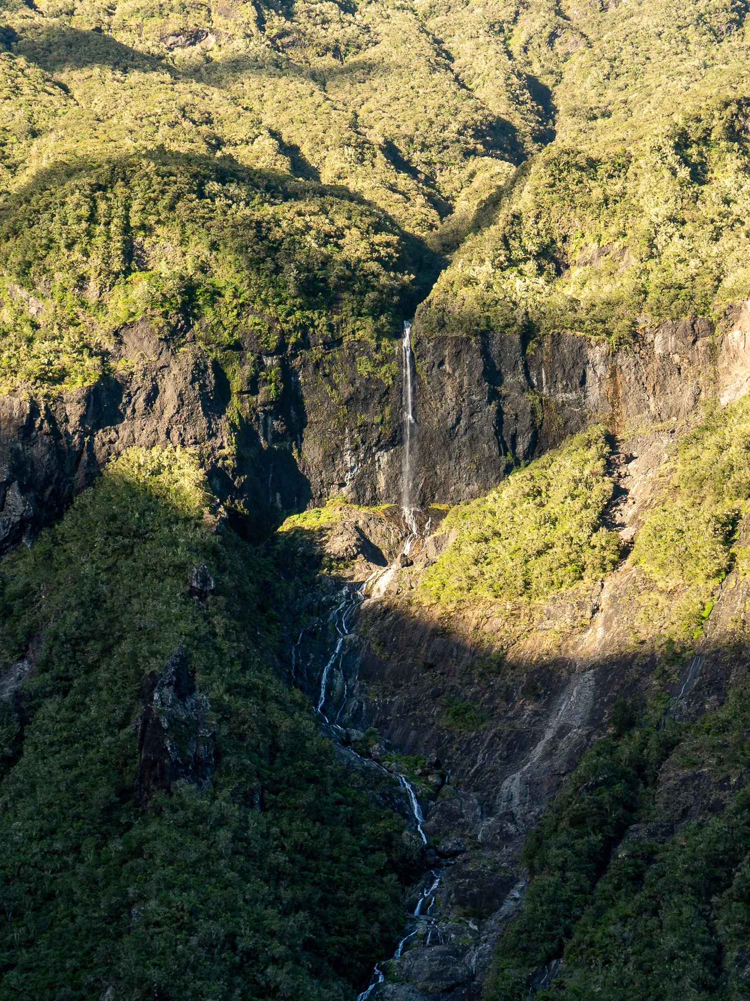 Wasserfall fällt in einen tiefen Schluchtengraben zwischen bewaldeten Hängen.