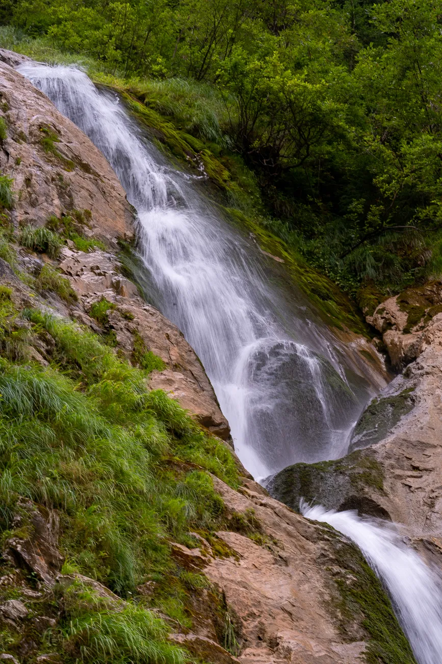 Wasserfall fließt über steinige Böschung mit grünem Moos und Vegetation