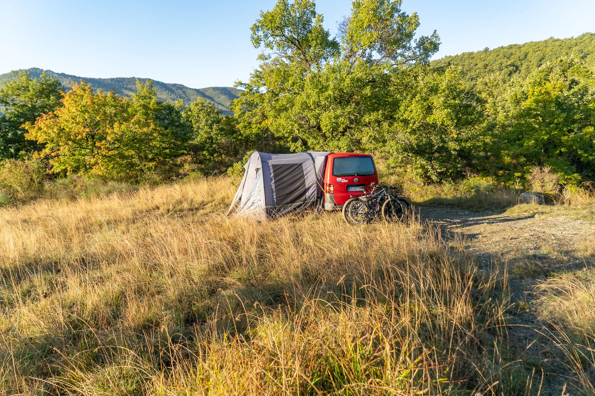 Zelt neben rotem Auto und Fahrrad im Gras bei Sonnenuntergang